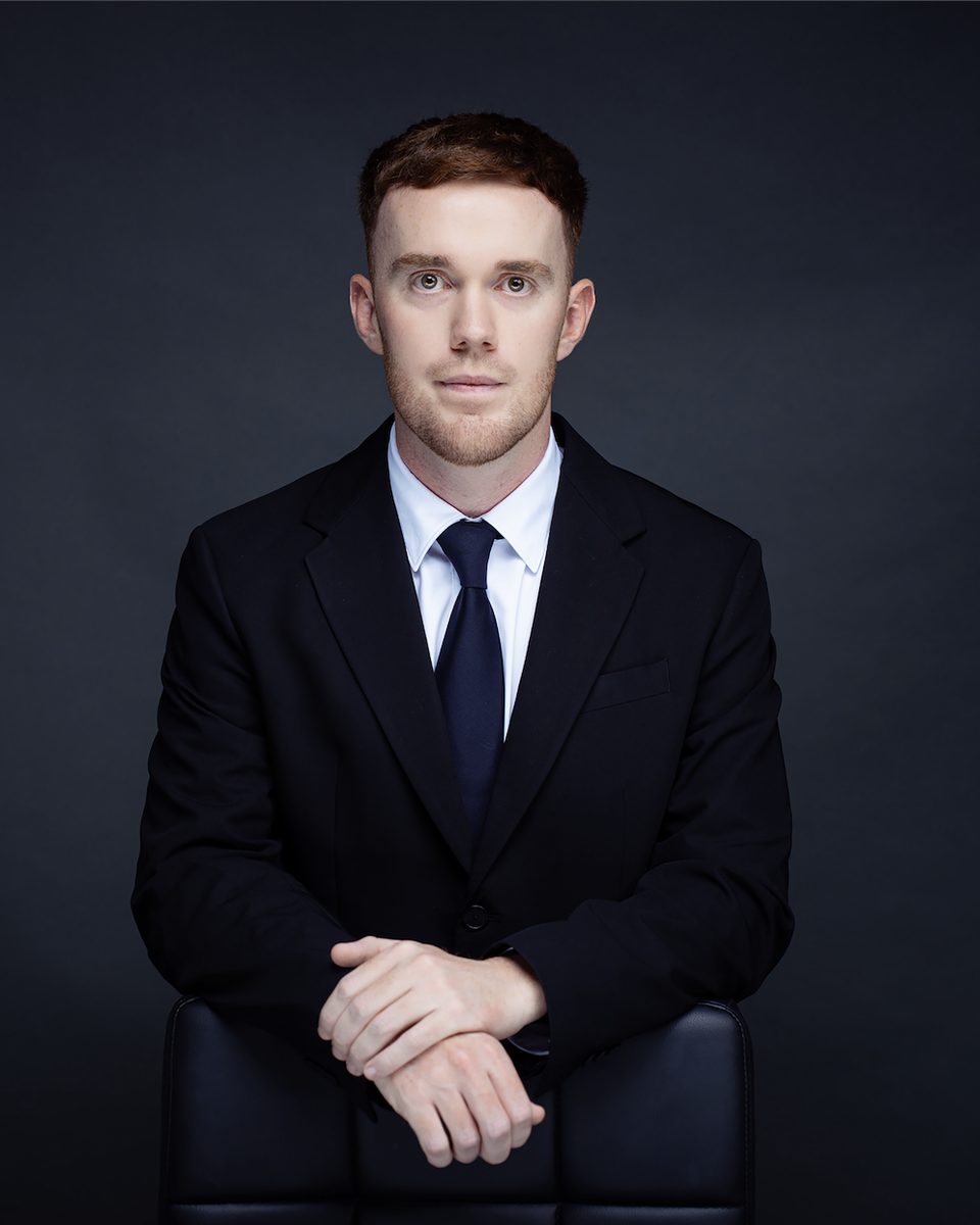 Daniel Legg, seated, in a dark suit and navy tie